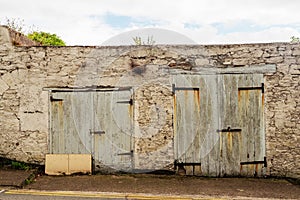 Two old weathered garage or small warehouse doors in an old building. Nobody. Vegetation grows on the roof of the building