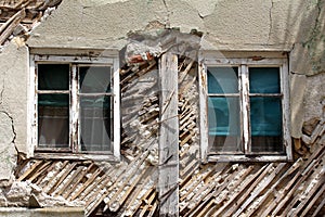 Two old windows with cracked white wooden frames on abandoned suburban family house ruins with destroyed walls