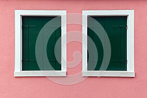 Two old windows with dark green shutters on light pink wall