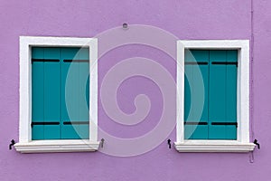 Two old windows with light blue shutters on light violet wall