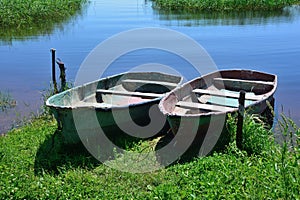 Two old wooden boats moored to the shore overgrown with green grass. On a bright summer sunny day