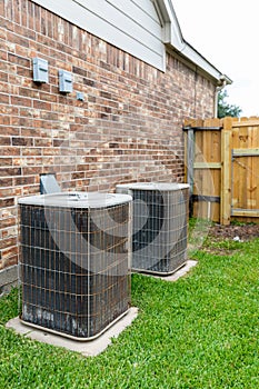 Two older air conditioner systems next to brick home with copy space