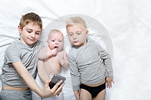 Two older brothers are lying with the youngest baby in a white bed. Happy childhood, big family