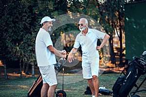 Older men stand on a golf course and talking