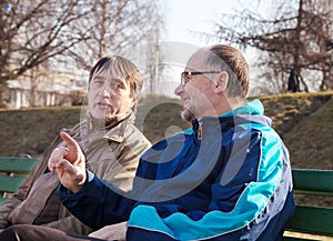 Two older men talk on a park bench