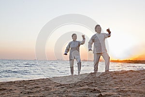 Two older people practicing Taijiquan on the beach at sunset, China