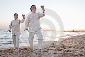 Two older people practicing Taijiquan on the beach at sunset, China