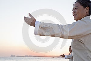 Two older people practicing Taijiquan on the beach at sunset, China