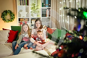 Two older sisters and their cute little baby brother having fun together in a cozy living room on Christmas eve. Kids spending