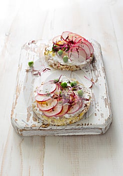 Two open sandwiches with radish, green peas, soft cheese and micro greens