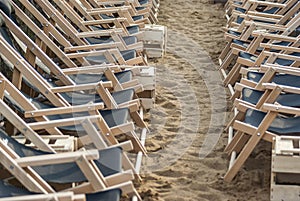 Two opposing rows of suspended empty deck chairs in rows lined up in order on the beach in the sand