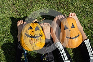 two orange pumpkins with painted grins and the bare feet of two children sitting on the grass photo