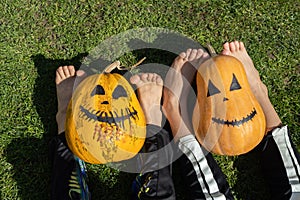 two orange pumpkins with painted grins and the bare feet of two children sitting on the grass