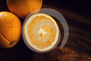 Two oranges, one halved to reveal juicy segments, on a dark wooden backdrop