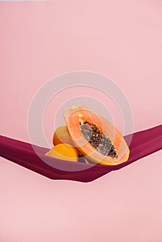 two oranges and a papaya cut in half on a red cloth in front of a peach background as a symbol of the pelvic floor photo