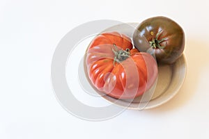 Two organic heritage tomatoes crowded onto a shallow dish, align