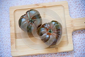 Two organic tomatoes on a wooden cutting board