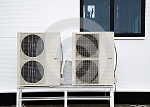 Two outdoor units of air conditioners standing on the ground in front of facade of the modern building