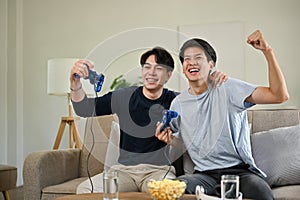 Two overjoyed Asian male friends raised their hands, celebrating their game wins
