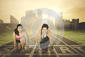 Two overweight women kneeling on the start line