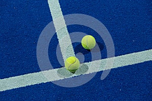 Two paddle tennis balls in the foreground on the line of a blue paddle tennis court at night