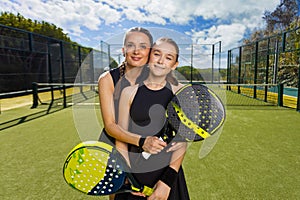 Two padel tennis players with rackets. Woman and girl teenager athlete with paddle racket on court outdoors. Sport
