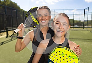 Two padel tennis players with rackets. Woman and girl teenager athlete with paddle racket on court outdoors. Sport