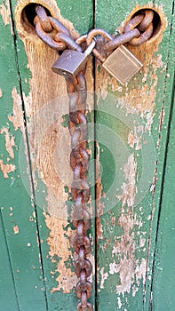 Two Padlocks and Chain on Green Doors With Worn Paint