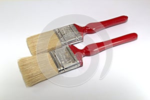 Two paint brushes 2 inches wide with red handles on a wooden background