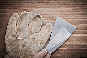 Two paint scrapers and safety gloves on wood board