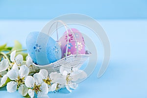Two painted blue and purple Easter eggs in basket with white spring cherry flowers on light blue background