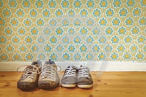 Two pair of old dirty shoes in front of retro wallpaper