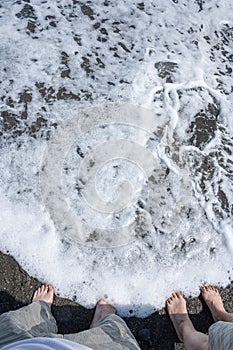 two pairs of bare feet of a man and a woman in the surf foam