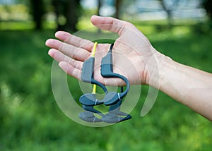 Two pairs of bone conduction sports headphones. Hand holding audio devices on soft green background.