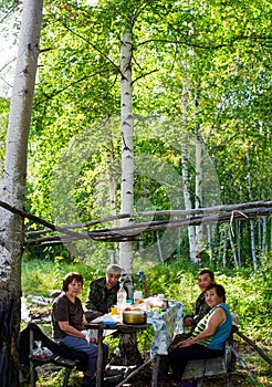 Two pairs of elderly Yakuts sit at a table with food in a place to rest in the wild taiga of the birch forest