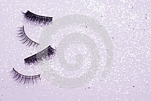 Two pairs of false eyelashes on a trendy pastel pink background with sparkles. Beauty pattern. Makeup accessories. Cosmetics