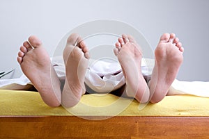 Two pairs of feet in bed photo