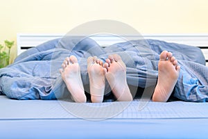 Two pairs of feet of kids. Brother and sister lying under blanket