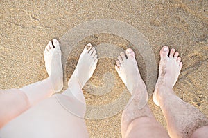 Two pairs of feet, male and female crossed on a sea beach sand. Concept of summer vacation