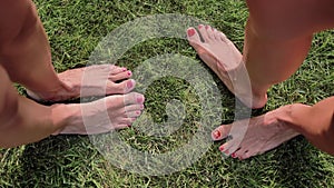 Two pairs of female feet stand opposite each other on the green grass