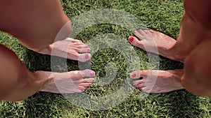 Two pairs of female feet stand opposite each other on the green grass