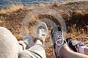 Two pairs of female legs in sports sneakers on the seashore. Female feet seen from above