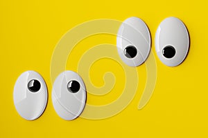 Two pairs of funny googly or wiggle eyes looking towards each other on yellow background, minimal concept