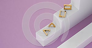 Two pairs of golden modern earrings on white podium on purple geometric background with copy space