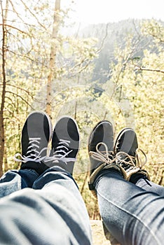 Two pairs of legs in boots against a background of trees