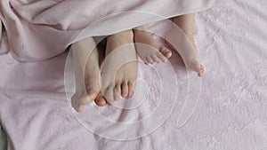 Two pairs of legs of the family in bed under the coverlet - mother and baby