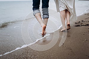 Two pairs of legs of lovers walk on the sand on the seashore.