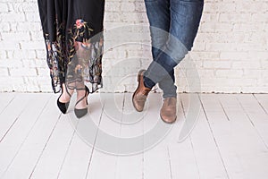 Two pairs of male and female legs in shoes are crossed. Couple standing in front of the white wall crossed-legs in shoes. Girl in