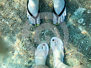 Two pairs of male and female legs in slippers, feet with fingers in flip-flops under the water, underwater view of the sea, the oc