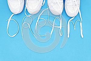 Two pairs of matching white sneakers with the lettering DREAM made of the laces on a blue background.